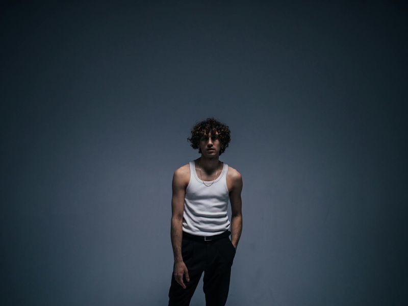 A man in athletic wear performing a slow, controlled bodyweight movement in a minimalist dark room.